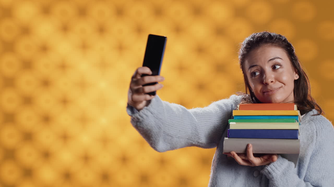mujer alegre con una pila de novelas en los brazos haciendo selfies, fondo de estudio