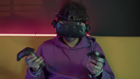 boy playing video games wearing virtual reality glasses and using gamepads sitting on sofa at home