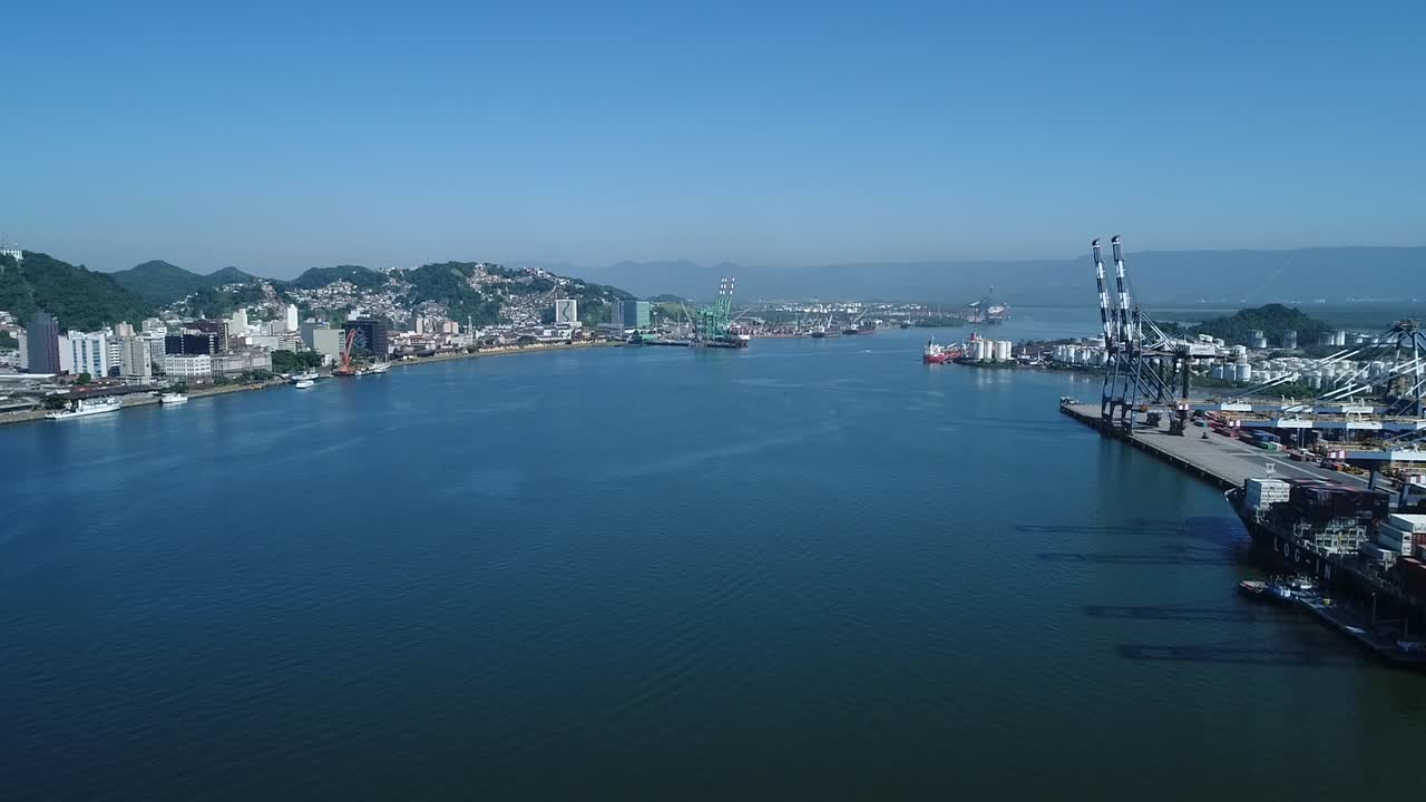 Drone filming in the middle of the channel of the largest port in latin america, intense maritime trade, cargo handling, sunny blue day