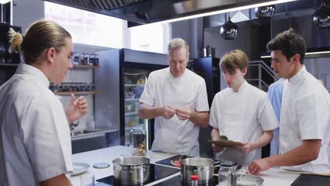 professional caucasian male chef in a restaurant kitchen teaching male trainee chefs