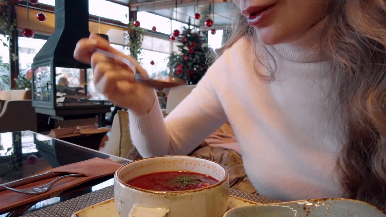 Brunette woman eating borscht at a restaurant decorated for Christmas