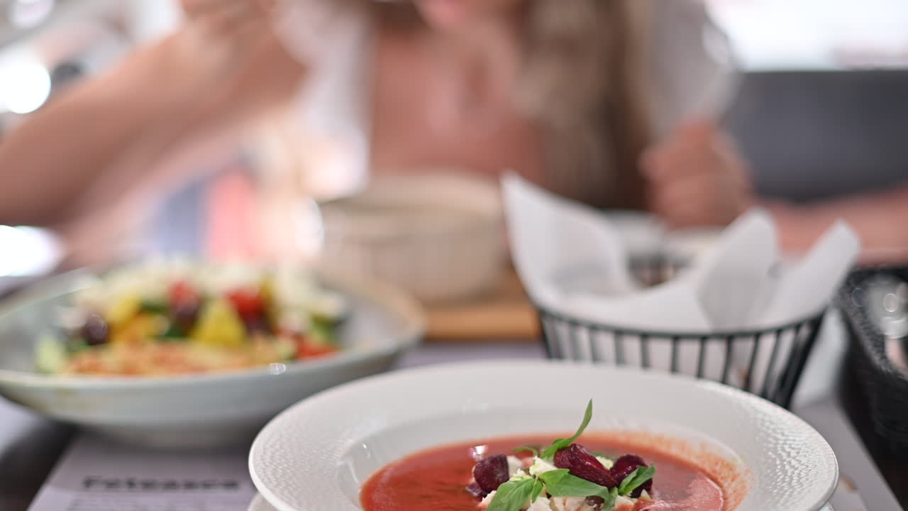 Primo piano di diversi tipi di cibo su un tavolo in un ristorante con una donna che mangia sullo sfondo