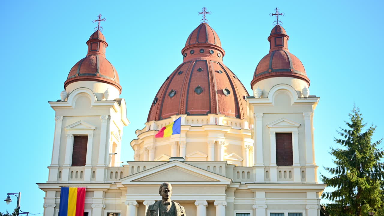 Iglesia de la Anunciación y estatua de Emil Dandea en el centro de Târgu Mureș, Rumanía. Flores y vegetación.