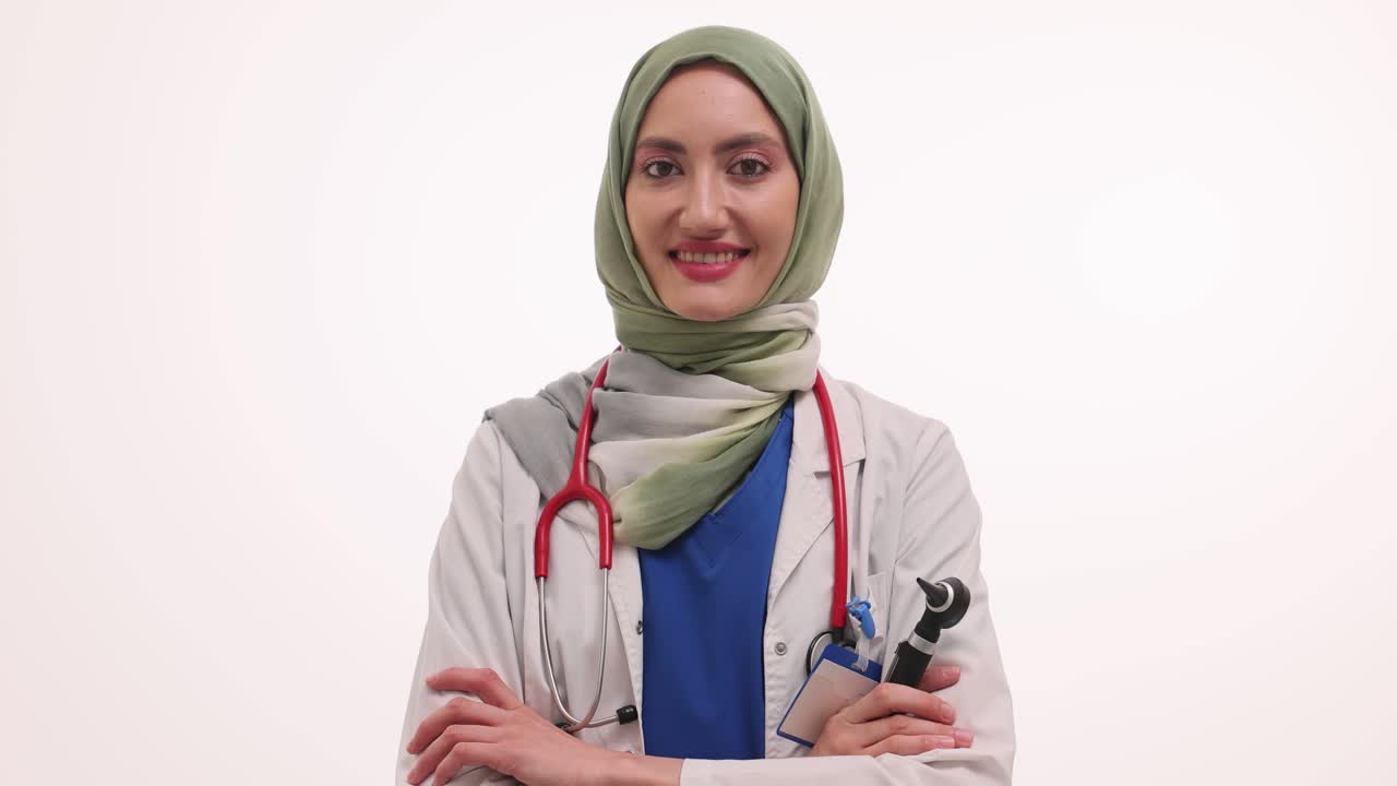 A confident female doctor in a hijab, white coat, and stethoscope, holding an otoscope, smiling at the camera