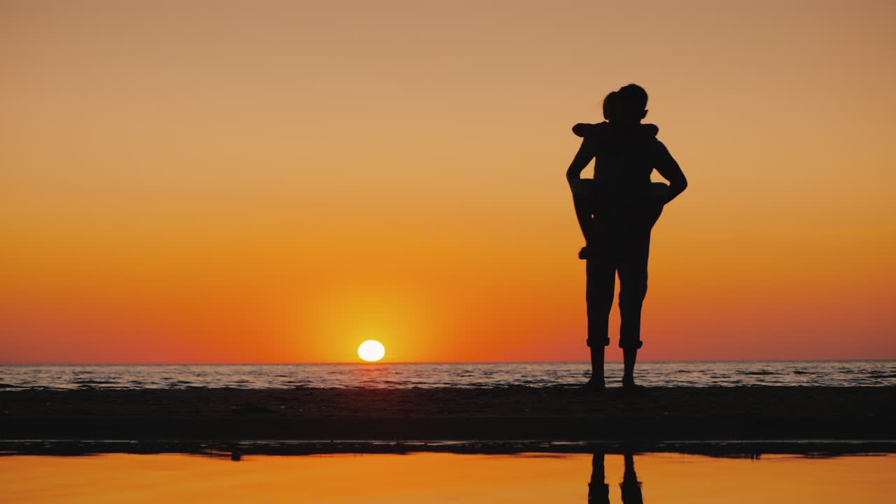 A Young Man Plays With A Child Carries Him On His Shoulders On The Beach
