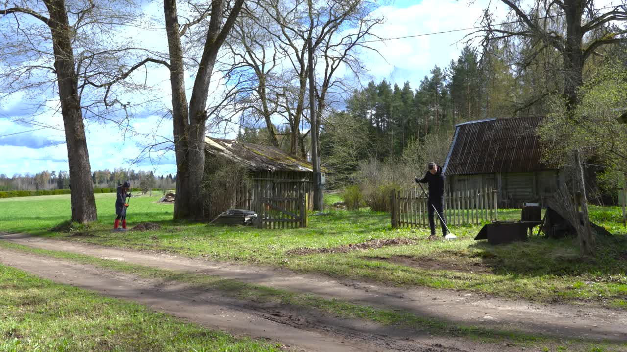 Gorgeous footage of people raking leaves in a sunny and cloudy countryside garden in timelapse or hyperlapse mode. People are cleaning yellow fallen leaves from green grassy mowerd lawn yard.