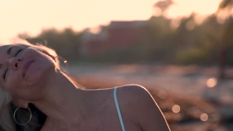 Portrait-of-beautiful-backlit-mature-woman-with-gray-hair-on-a-tropical-beach-looking-at-camera-and-moving-her-hair-over-to-the-other-side