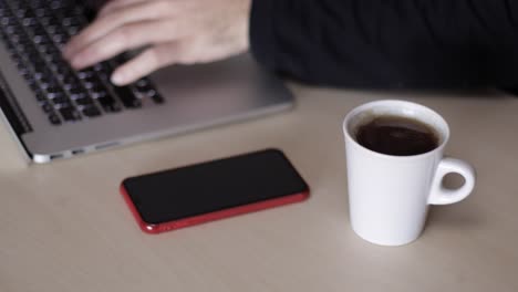 slow motion: man works on laptop in the office having a cup of tea