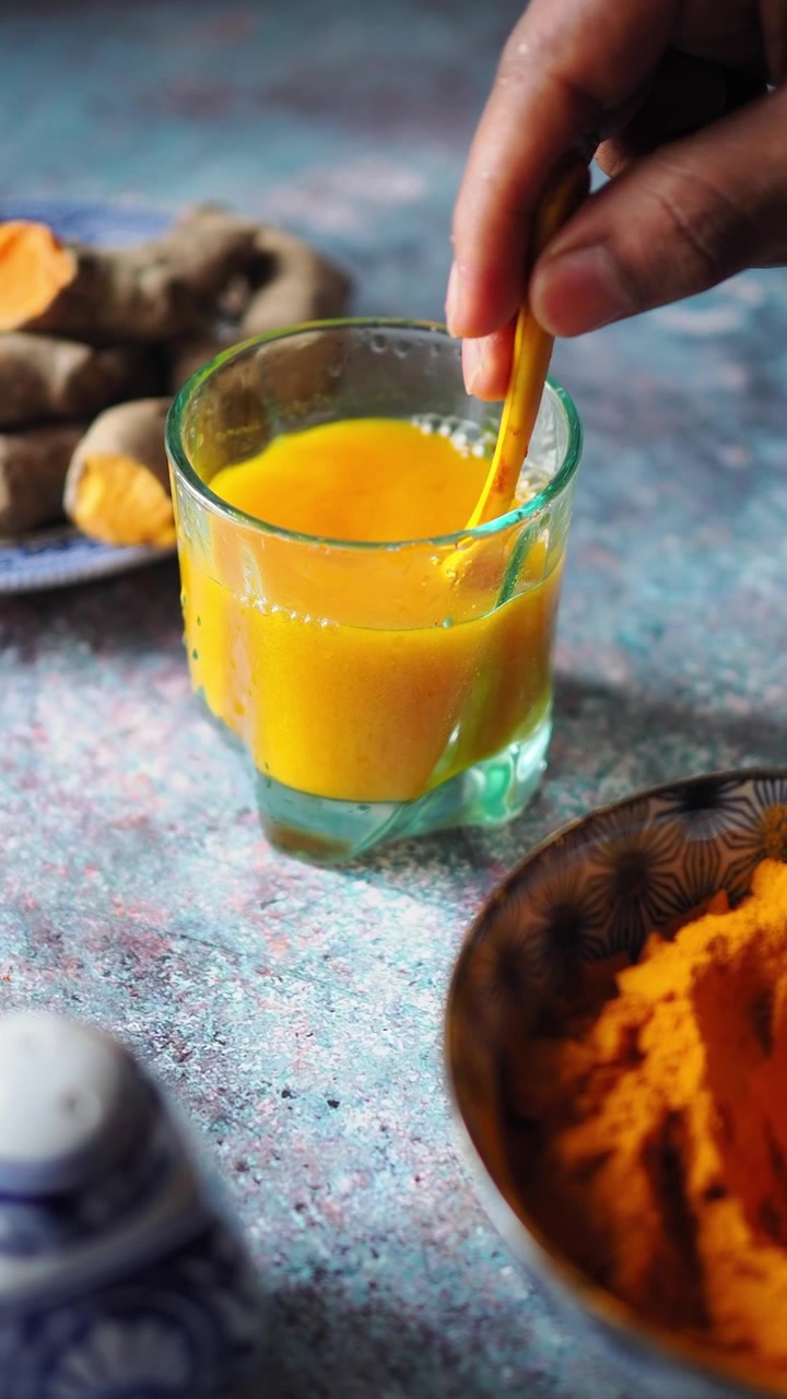Hand Stirring Fresh Turmeric Drink in a Glass