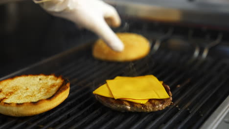 hands of a person fry buns on grill. meat cutlet with cheese on top. fast food concept.