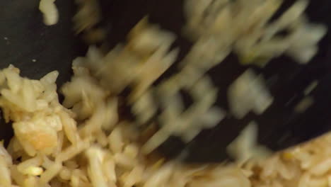 Overhead-detail-view-of-yellow-white-raw-rice-cooking-in-black-skillet-and-mixed,-stirred-and-rotated-with-plastic-spatula,-macro-static-extreme-close-up