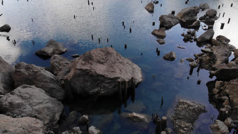 Drone-Volando-Sobre-Una-Pareja-Sentada-Al-Borde-De-Un-Acantilado-Junto-A-Un-Lago