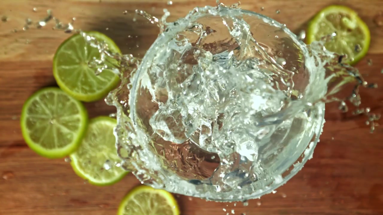 Cubetti di ghiaccio al rallentatore che schizzano in un bicchiere da cocktail con lime