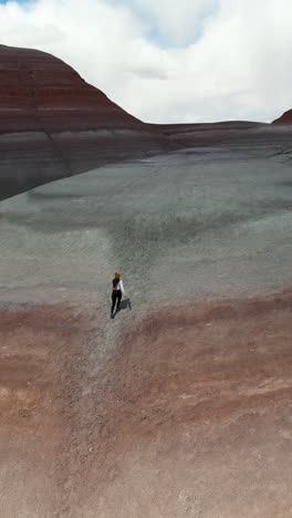 vertical aerial view of woman running alone to the top of hill with layers of sandstone, drone shot