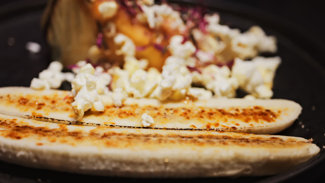 Close up of a cheesecake with a banana split and caramelised popcorn on a black plate at a restaurant