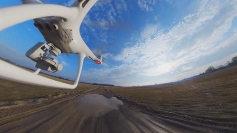 close-up side view of dji phantom 4 quadcopter drone flying forward over a country gravel road