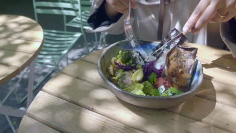 a bowl of colorful food being eaten at an outdoor table