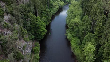 Aerial-drone-view-of-kayaking-through-river-surrounded-by-forests