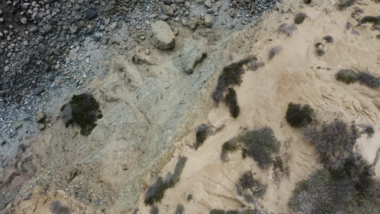 надир кукольный аэрофотоснимок пролетает над склоном скалы, показывая темные океанские волны, разбивающиеся о берег и о скалы, и множество морских худу и морских стогов