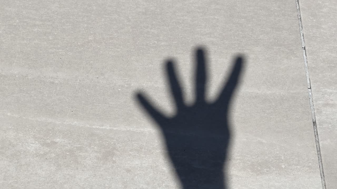A dark hand shadow counts from one to five against a textured gray concrete wall