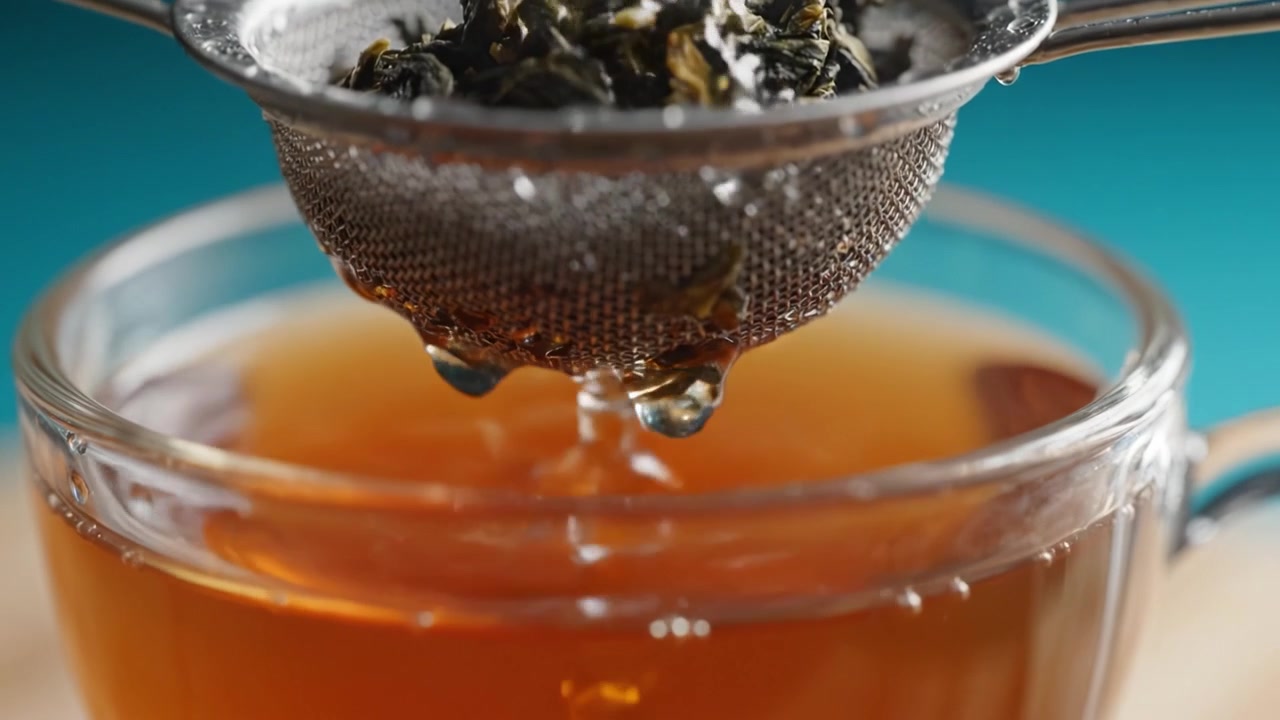 Preparazione del tè verde: Uno sguardo ravvicinato al processo di infusione con foglie di tè in infusione in un colino sopra una tazza di vetro piena di tè aromatico.