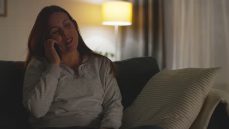 Close-Up-Of-Smiling-Woman-Sitting-On-Sofa-At-Home-At-Night-Talking-On-Mobile-Phone-3