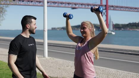 smiling blonde girl doing exercises with dumbbells in park.