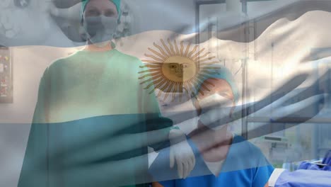 Animation-of-waving-argentina-flag-over-caucasian-male-and-female-surgeon-at-hospital