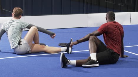 two diverse men resting on padel indoor court after intense match, catching their breath