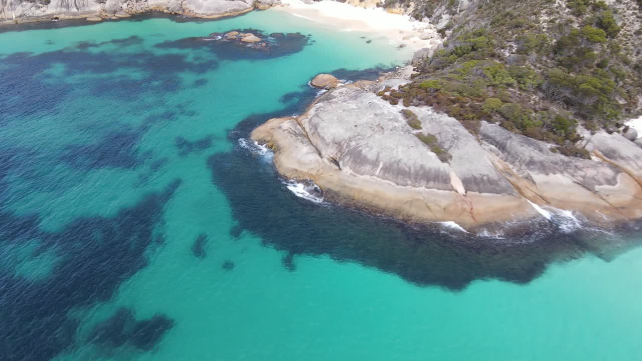 Ripresa aerea con drone che scende verso una spiaggia appartata con sabbia bianca e acqua blu