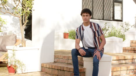 Biracial-man-smiling-and-sitting-on-front-stairs-outdoors,-slow-motion