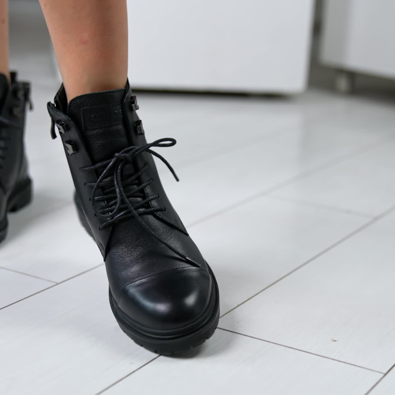 Bare-legged model demonstrating low black leather boots with laces. Woman rises foot to shoe the tractor sole of footwear. Close up
