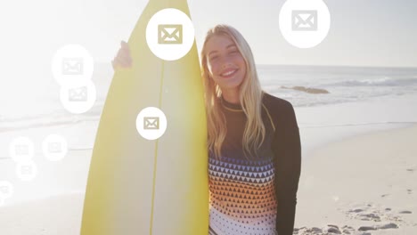 Animation-of-social-media-email-icons-over-smiling-woman-holding-surfboard-on-beach