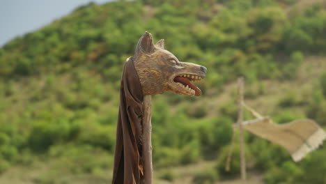 a cinematic, low-angle shot orbits the iconic dacian draco. the camera circles the bronze wolf-headed battle standard, revealing its fierce details against the sky