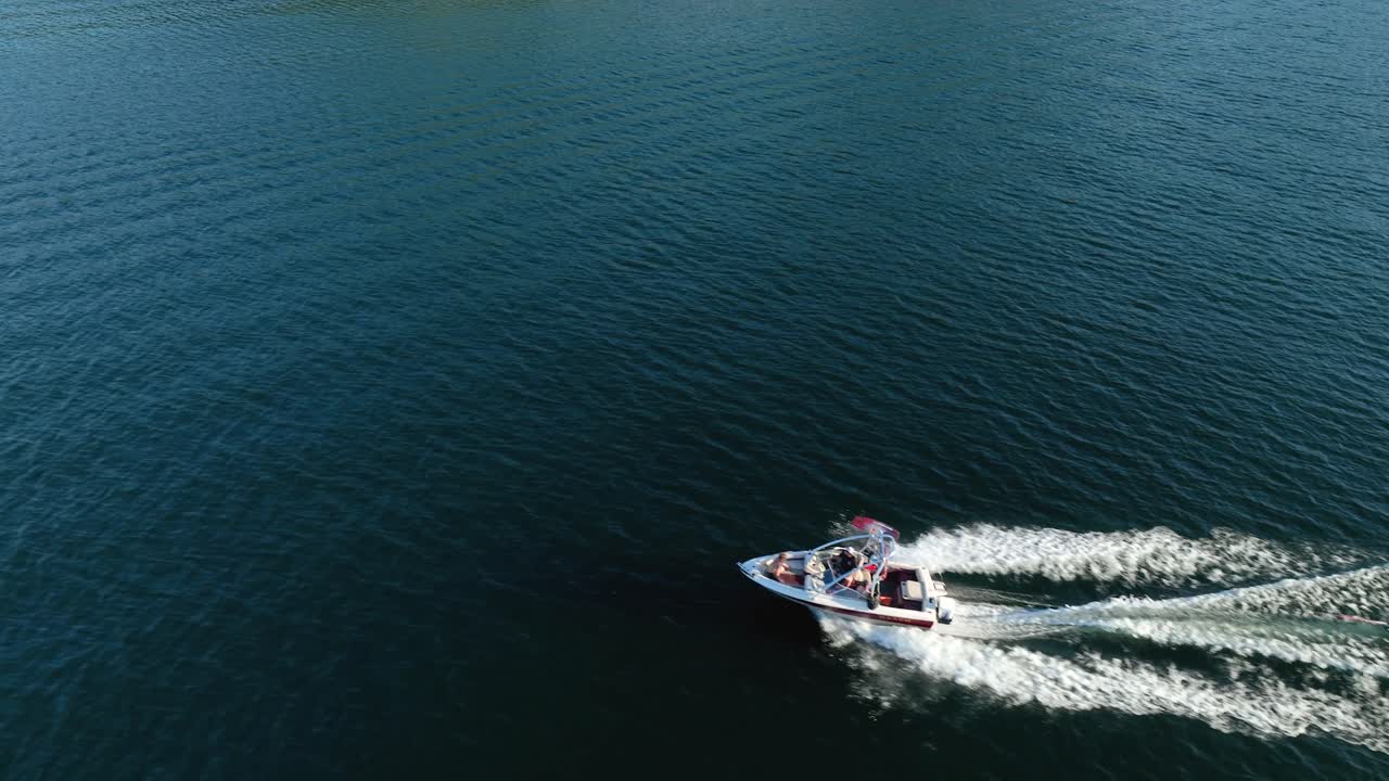 Rising drone shot of person skiing behind a motorboat
