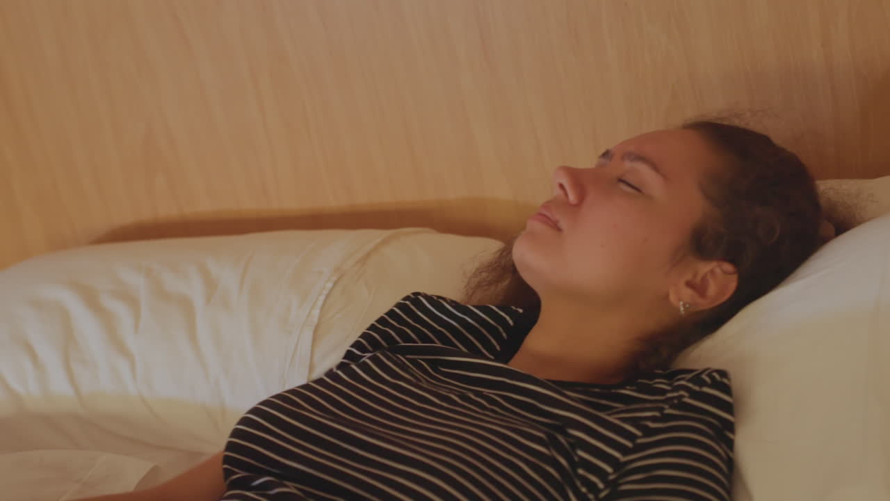 Kvinde kæmper mod fredelig søvn. Hotelgæst kæmper for hvilefuld søvn. Træt kvinde i hotelseng kæmper for at finde komfort. Søvnen undviger kvinden i hotelværelset, da hvilen er uopnåelig.