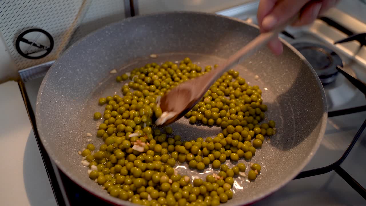 Mixing Frying Garlic And Peas With A Wooden Spoon On A Cooking Pan