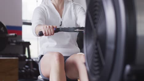 video de una mujer caucásica decidida usando una máquina de remo trabajando en el gimnasio