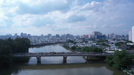 Aerial-tracking-shot-of-urban-traffic-bridge-and-high-density-waterfront-housing-along-a-canal-in-Ho-Chi-Minh-City,-Vietnam-in-afternoon-light
