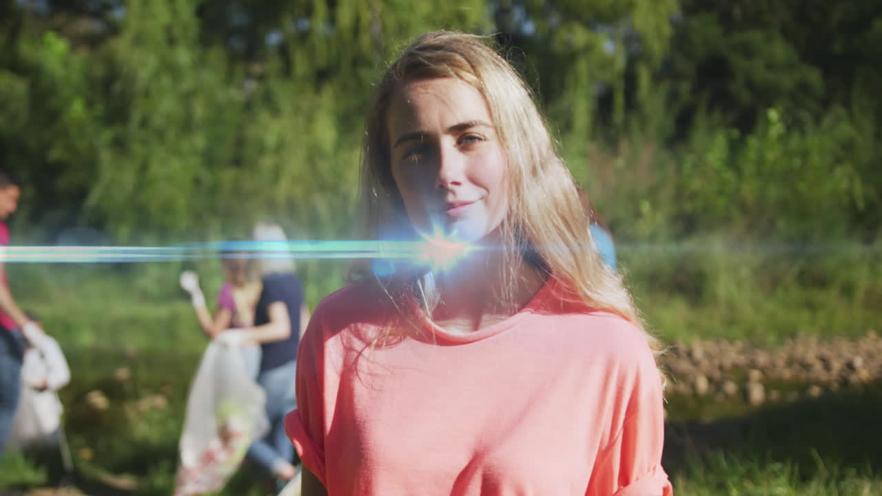 video de luces sobre una feliz mujer caucásica recogiendo basura con voluntarios en el campo