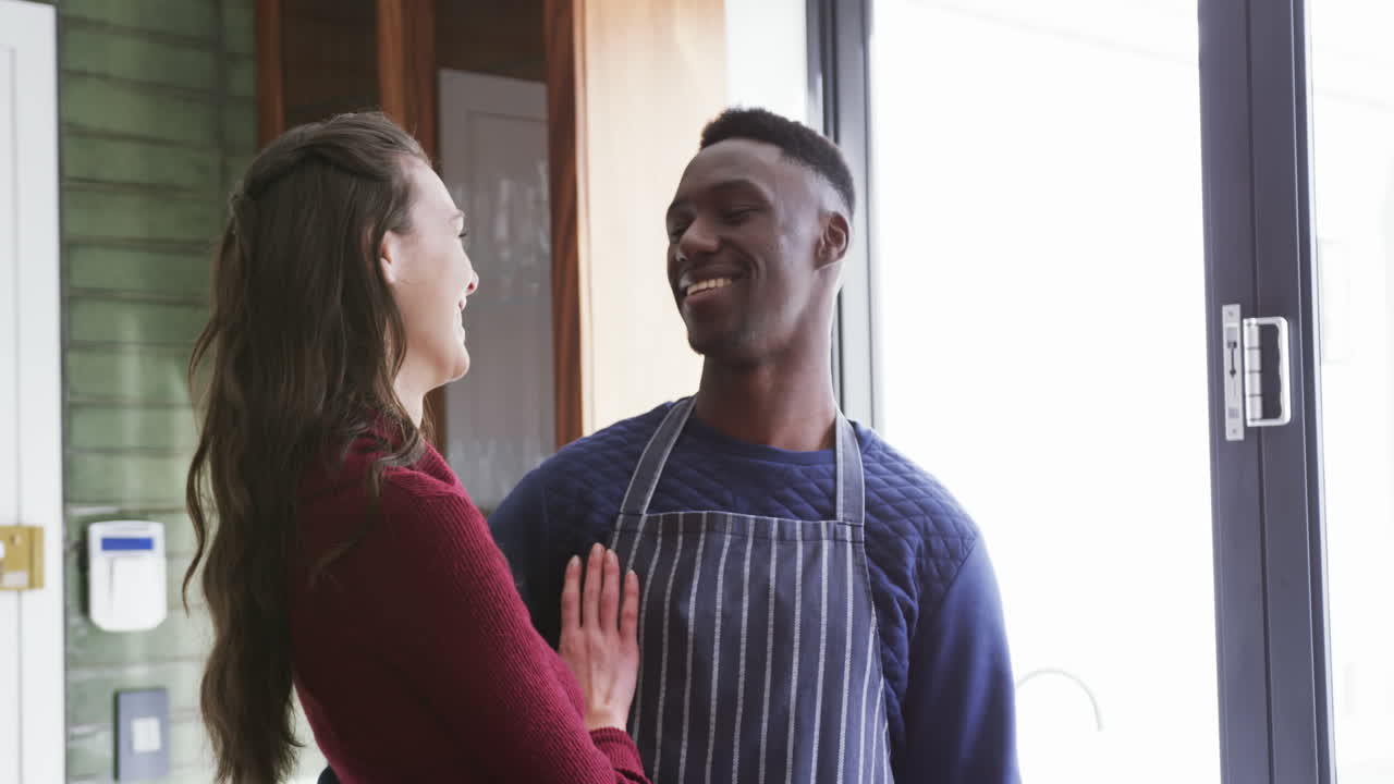 una pareja feliz y diversa de pie en la cocina, sonriendo y abrazándose, en cámara lenta.