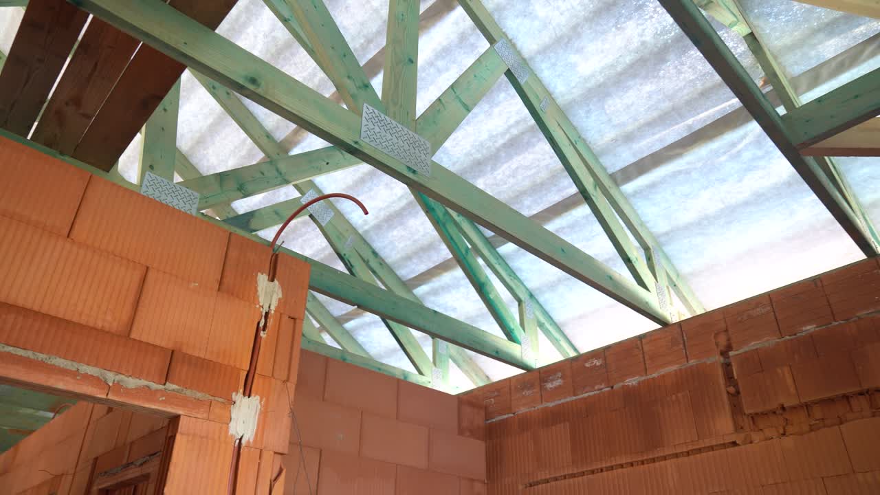 Exposed timber roof trusses above unfinished brick walls inside house under construction