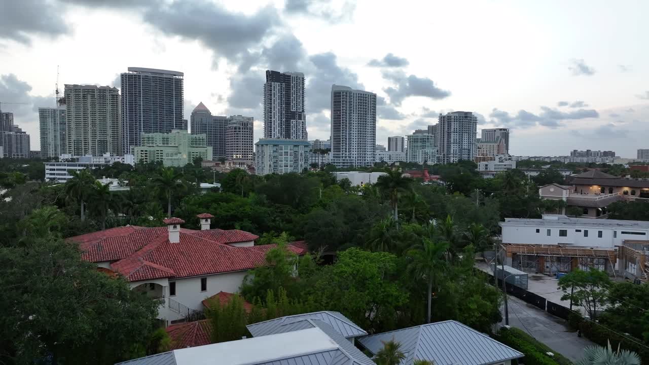 Modern waterfront mansion in Fort Lauderdale. Sleek design and infinity pool with canal access. Aerial rising shot revealing city skyscrapers. Luxury living and urban proximity.