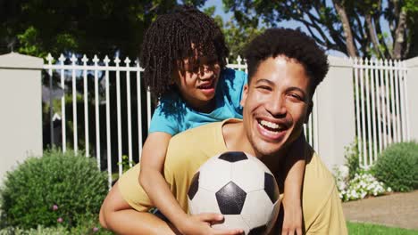 Porträt-Eines-Glücklichen-Gemischtrassigen-Mannes-Und-Seines-Sohnes,-Der-Im-Garten-Fußball-Spielt