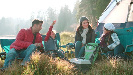 parents with two kids on a camping trip sitting outside tent