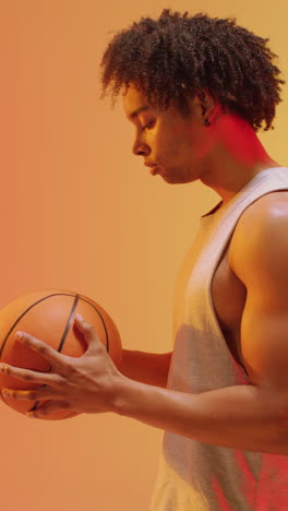 video vertical de un jugador de baloncesto masculino biracial con una pelota en un fondo naranja