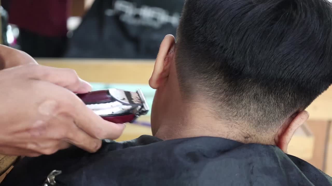 Ragazzo asiatico di spalle mentre si fa acconciare i capelli in una moderna barberia.