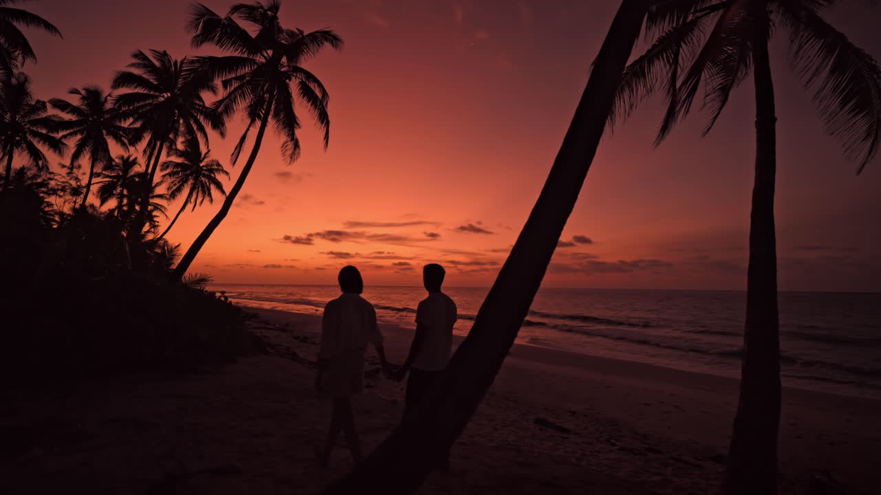 A heartwarming scene unfolds as a couple strolls hand in hand along the pristine sands of Geiymiskih Fannu beach in Fuvahmulah, Maldives at sunset.