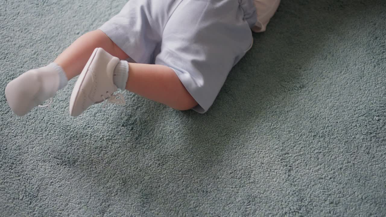 Baby lying on soft blue carpet, wearing light blue shorts and white shoes, capturing calm and comfortable moment