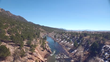 drone view of a green river in rocky ground with a bit of snow on the ground